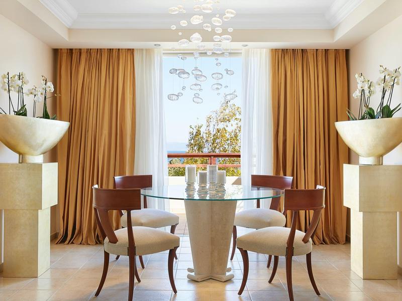 Elegant dining area with round glass table, wooden chairs, and large gold curtains.