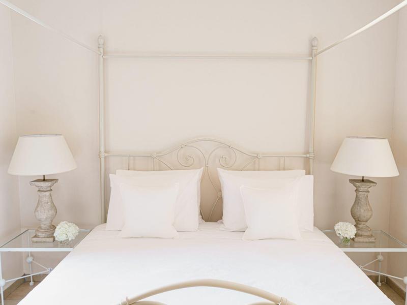Light, airy bedroom with a white four-poster bed, white pillows, and matching bedside lamps.