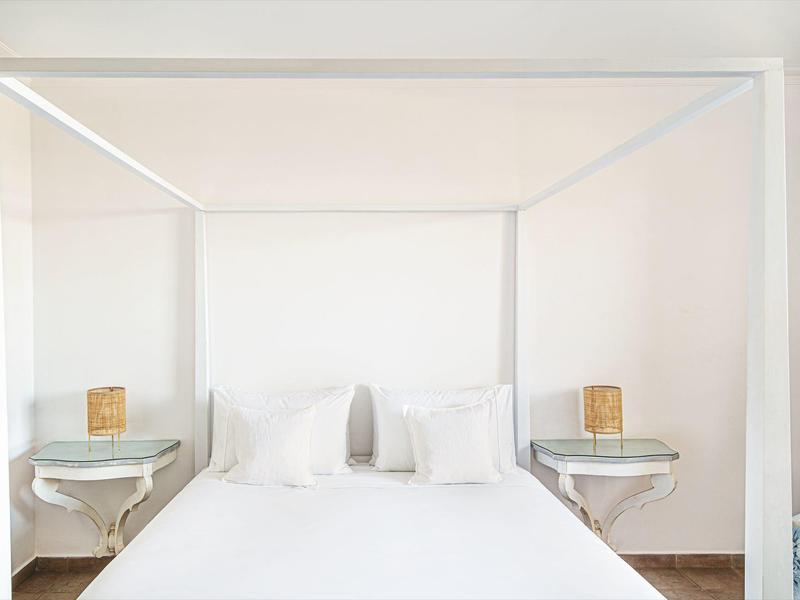 Brightly lit bedroom with white canopy bed and bedside tables with lamps.
