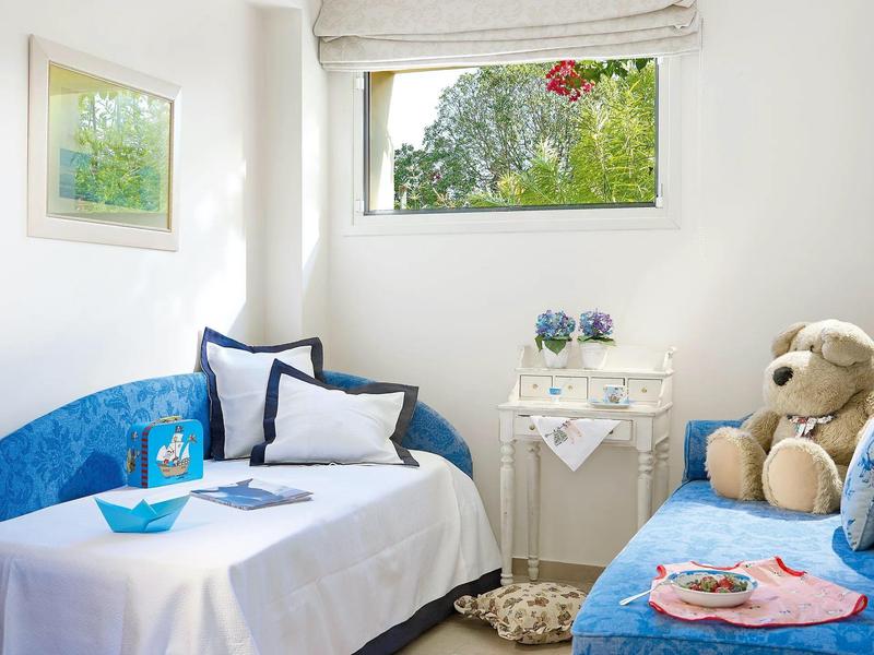 Bright hotel room with blue sofa bed, white linens, side table, and a large teddy bear.