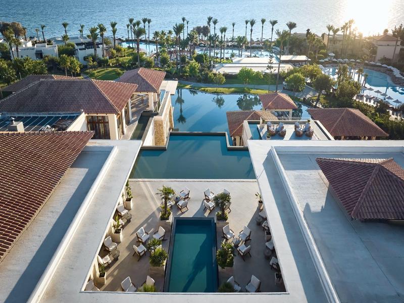 Luxury resort complex with multiple pools, sun umbrellas, and sea view at sunset.