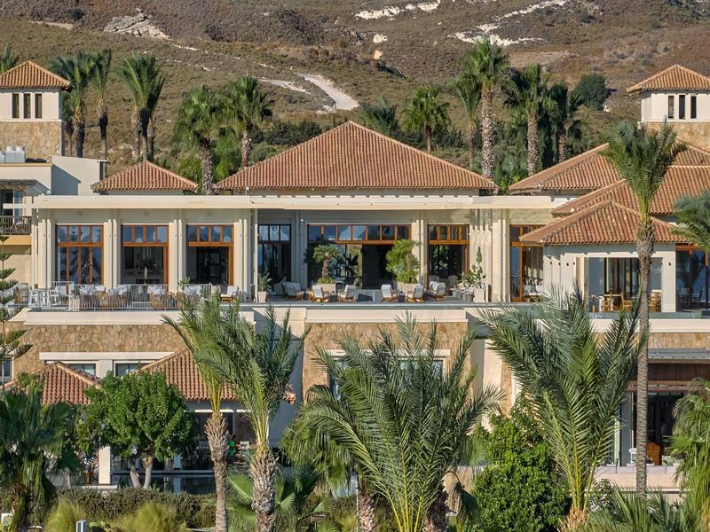 Large hotel building with terrace and tropical palm trees in front of hills.