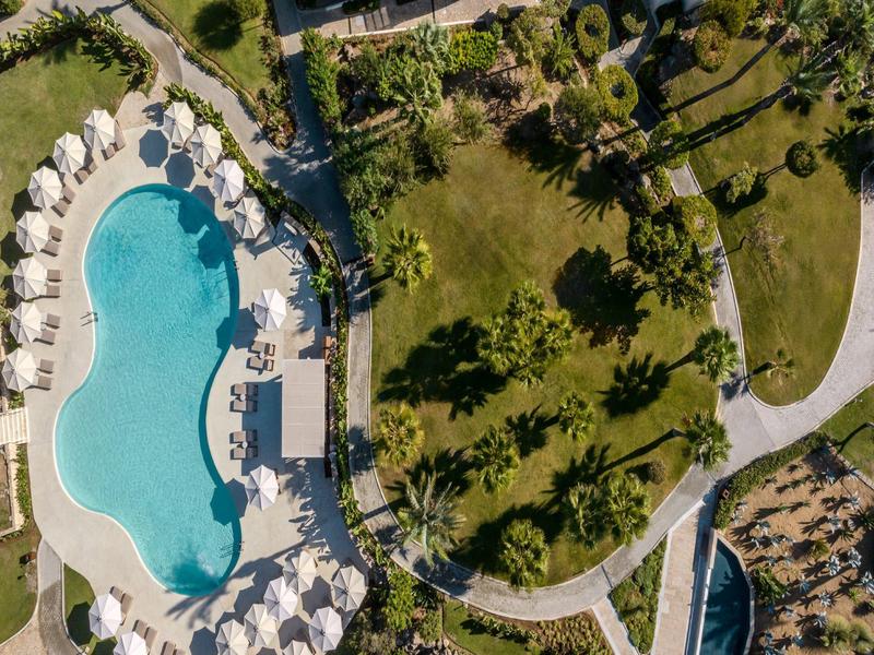 Aerial view of a hotel pool with lounge chairs and surrounding garden area.