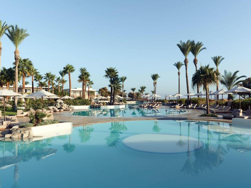 Large pool with palm trees and sun loungers under a clear sky at a resort.