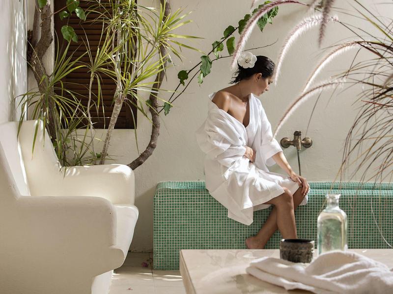 Woman in bathrobe sitting on green mosaic pool edge in relaxed spa setting.
