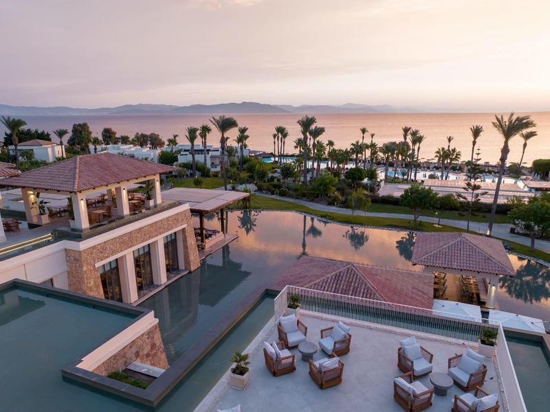 Luxurious hotel with pool and terrace, palm trees and sea view at sunset.