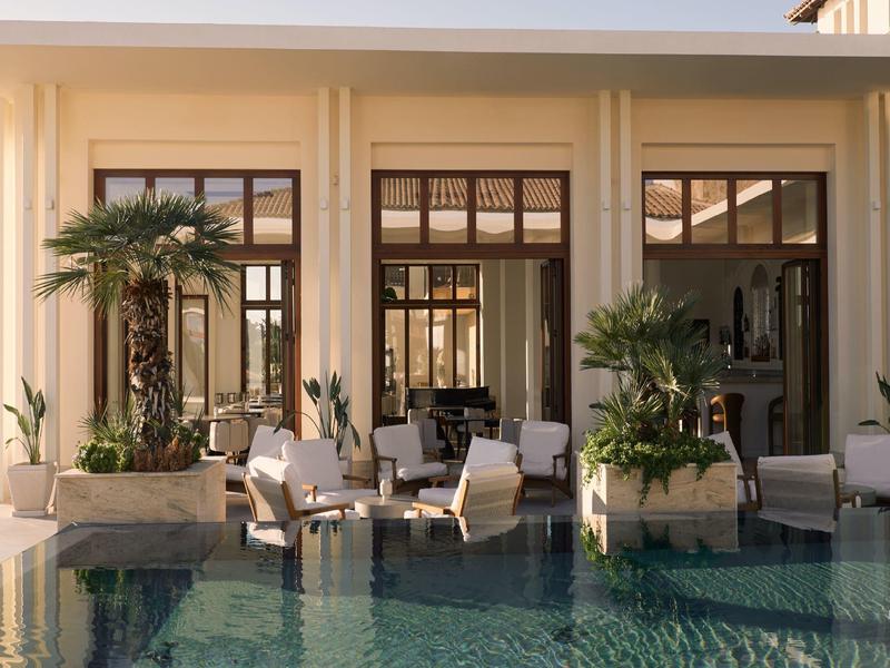 An elegant hotel pool with seating areas and plants along the facade in daylight.