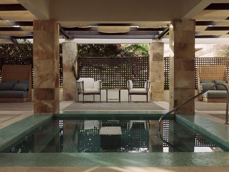 View of an indoor heated pool with white armchairs and wooden walls in the background.