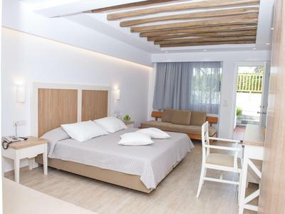Helles Hotelzimmer mit Doppelbett, Sofabereich, Holzbalkendecke und minimalistischer Einrichtung.