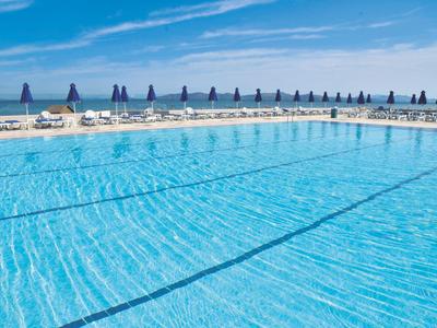 Großer Außenpool mit blauen Sonnenschirmen und Liegestühlen unter einem klaren Himmel.