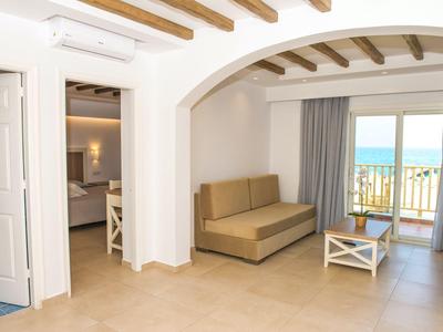 Helles Hotelzimmer mit Sofa, Stuhl, Tisch und Meerblick durch Fenster mit Balkon.