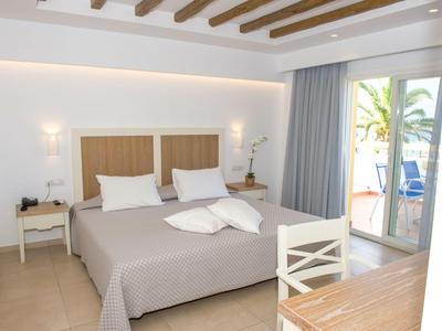 Helles Hotelzimmer mit Doppelbett, Holzmöbeln und Zugang zu Terrasse mit Meerblick.