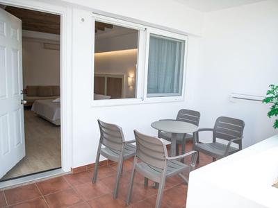 Balkon mit rundem Tisch und vier Stühlen vor einem Hotelzimmer mit offenem Tür