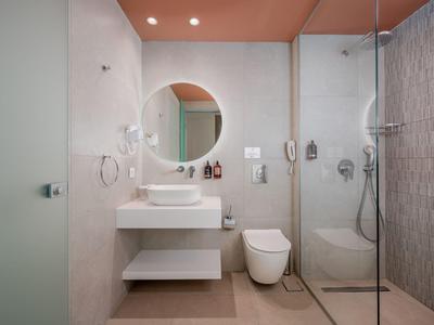 Moderner Hotelbadezimmer mit Dusche, Toilette, Waschbecken und runder Spiegel.