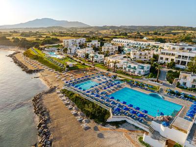 Resort mit mehreren Pools und Sonnenliegen direkt am Wasser in einer sonnigen Landschaft.