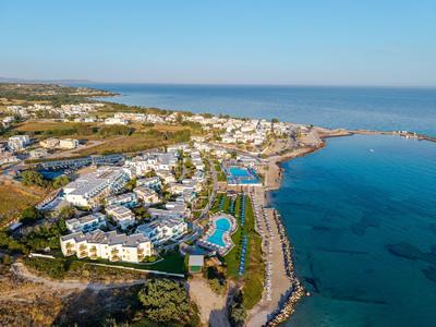 Blick auf ein Küstenhotel mit Schwimmbädern, grünen Flächen und Blick aufs ruhige blaue Meer.