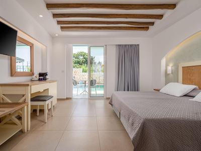 Helles Hotelzimmer mit Doppelbett, Holzbalken an der Decke und Zugang zum Balkon.