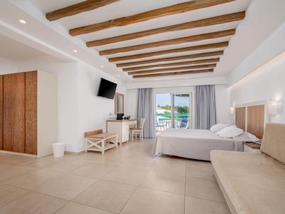 Helles Hotelzimmer mit Doppelbett, Sofa, Holzdeckenbalken und Meerblick vom Balkon.
