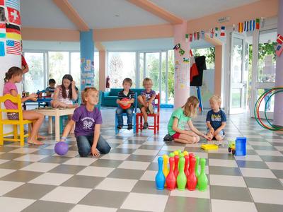 Kinder spielen in einem bunten, hellen Raum mit Fenstern und internationalen Flaggen.