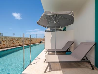 Moderne Liegestühle und Sonnenschirm neben einem schmalen Pool an einem Hotel.