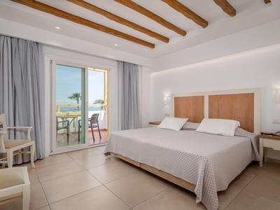 Helles Hotelzimmer mit Doppelbett, Holzbalken an der Decke und Balkon mit Meerblick.