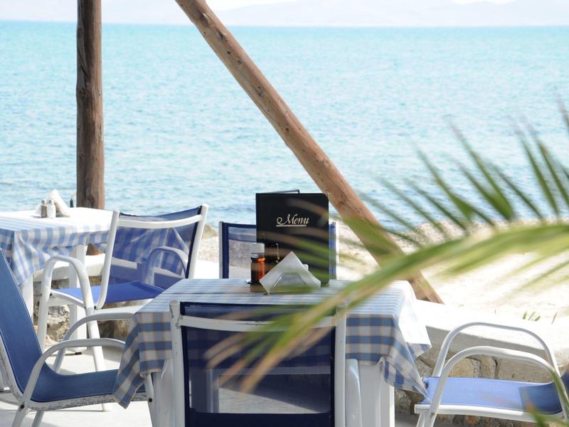 Terrasse mit blau-weißen Stühlen und Tischen am Strand mit Meerblick