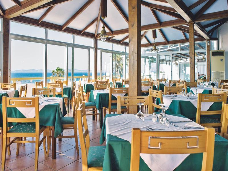 Helles Restaurant mit Holzmobiliar und Blick aufs Meer durch große Fenster