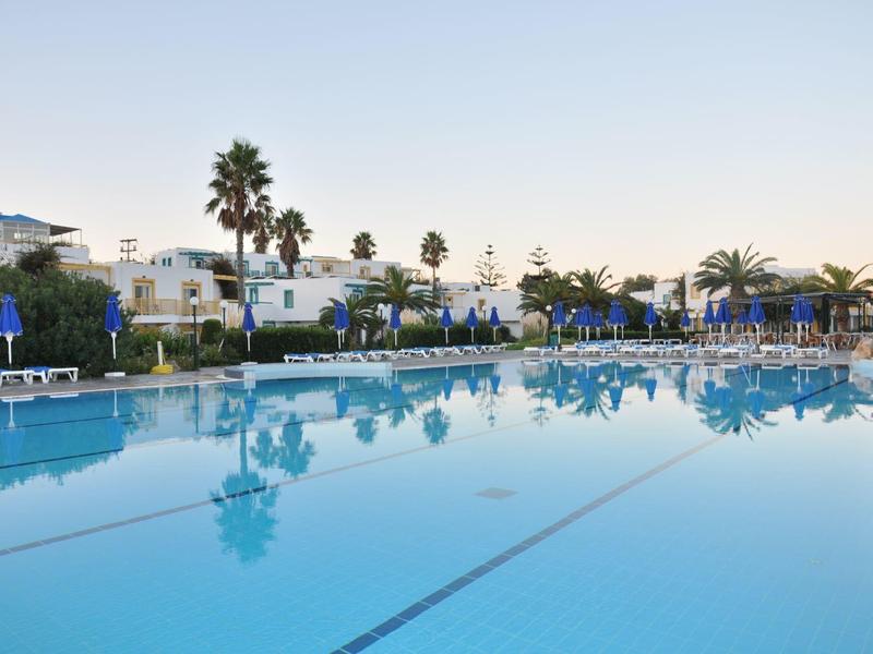 Großer Pool mit Liegestühlen und Palmen in einer Hotelanlage bei klarem Himmel.
