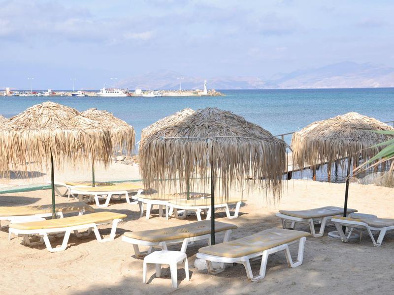 Leere Sonnenliegen mit Strohmachschirm am Sandstrand vor ruhigem blauem Meer