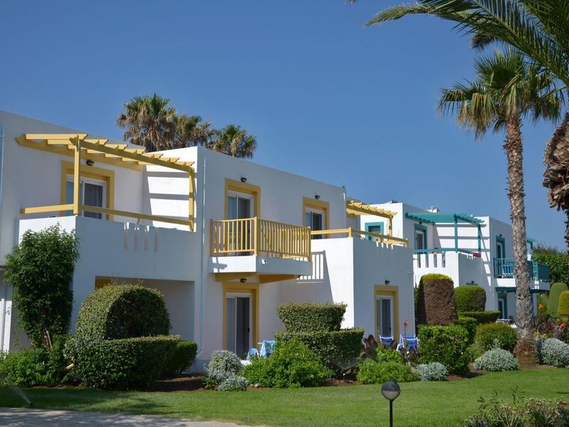 Weiße Ferienbungalows mit gelben Balkonen und gepflegtem Garten bei klarem Himmel