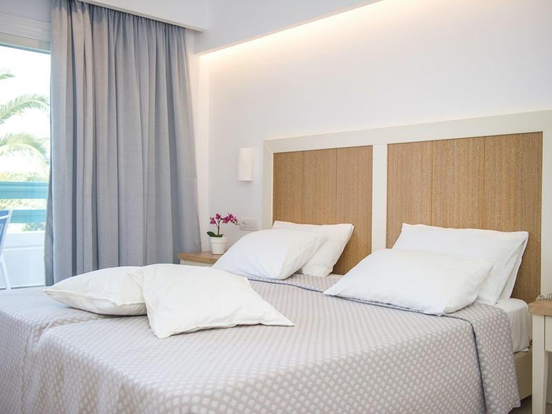 Modernes Hotelzimmer mit großem Bett, weißen Bettwäsche und Blick auf Palmen.