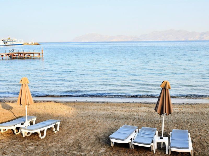 Leerer Strand mit Sonnenliegen und geschlossenen Sonnenschirmen am ruhigen Meer.