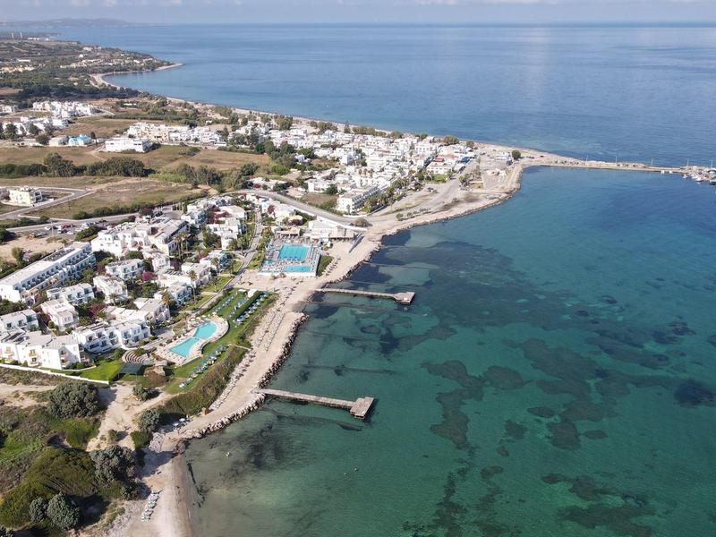 Luftaufnahme einer Küstenstadt mit weißen Gebäuden, Strand und klarem, blauem Wasser.