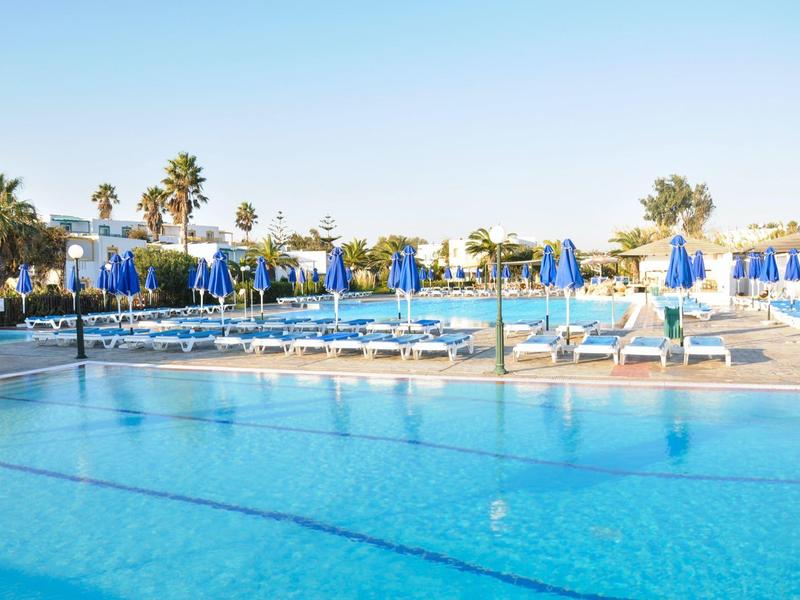 Großer Außenpool mit Liegestühlen und blauen Sonnenschirmen an einem sonnigen Tag.