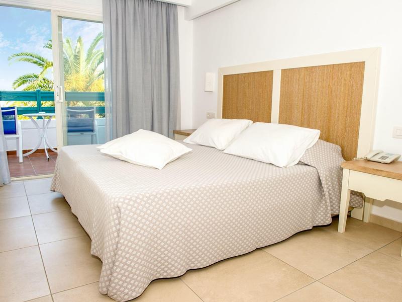 Helles Hotelzimmer mit Doppelbett, weißen Kissen und Balkon mit Meerblick.