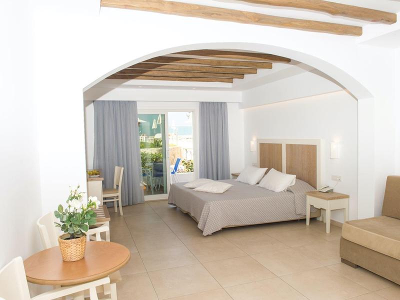 Helles Hotelzimmer mit Doppelbett, kleinem Esstisch und Sofa unter Holzbalkendecke.