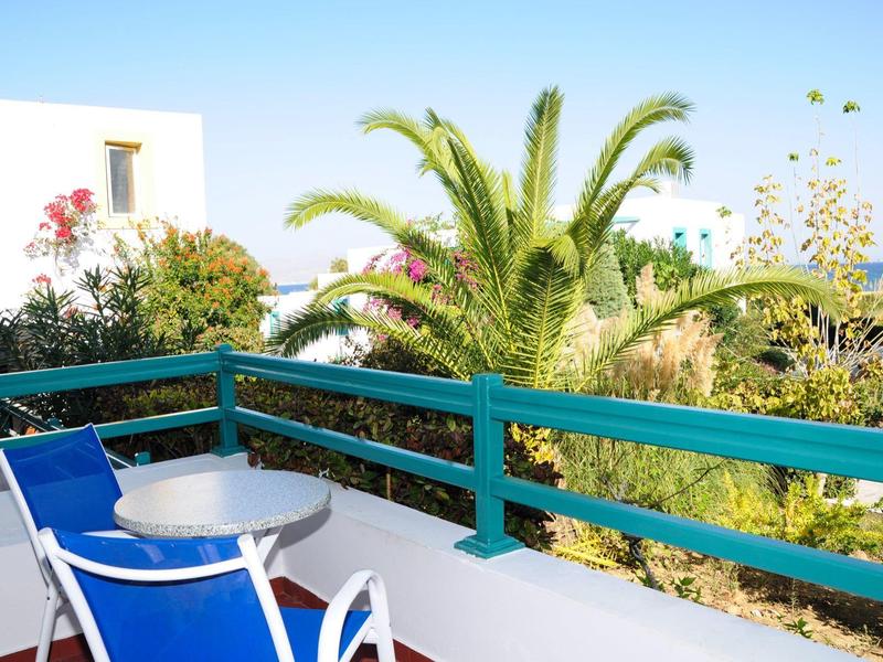 Balkon mit blauem Geländer, Tisch und Stühlen mit Blick auf Palmen und Gebäude.
