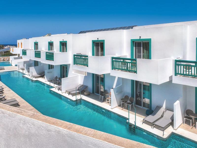 Moderne weiße Hotelzimmer mit direktem Zugang zum Pool und Sonnenliegen an einem klaren Himmel.