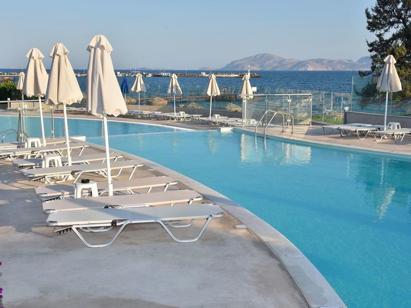 Leerer Poolbereich mit Sonnenliegen und geschlossenen Sonnenschirmen, Blick auf das Meer im Hintergrund.