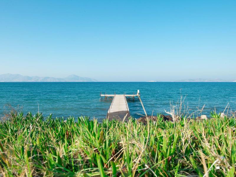 Grünes Gras im Vordergrund mit Blick auf eine Plattform am Meer unter klarem blauem Himmel