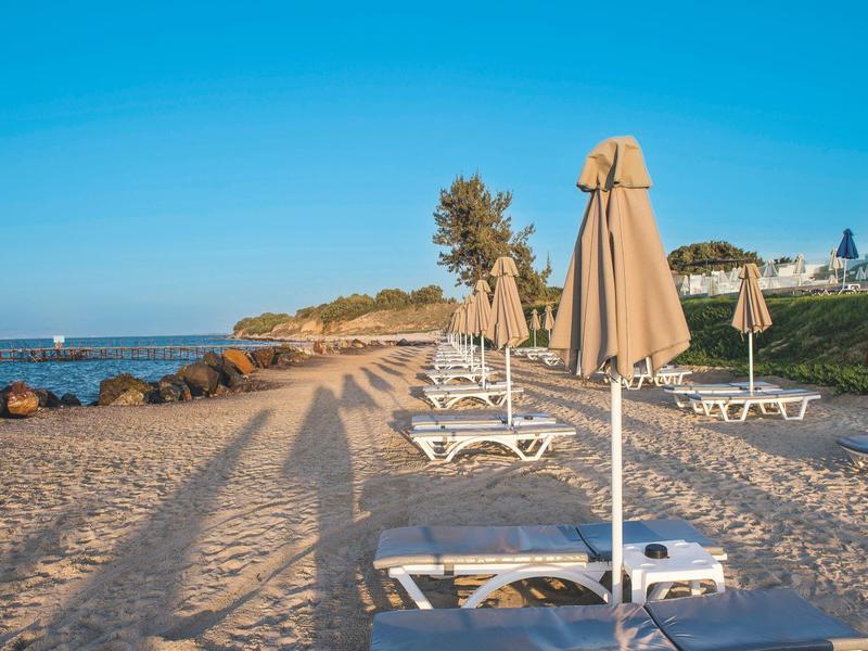 Leere Liegestühle mit geschlossenen Sonnenschirmen am Sandstrand bei klarem Himmel