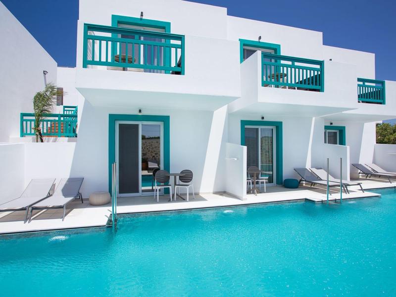 Weißes Gebäude mit blauen Balkonen und Außenpool in sonniger Umgebung.