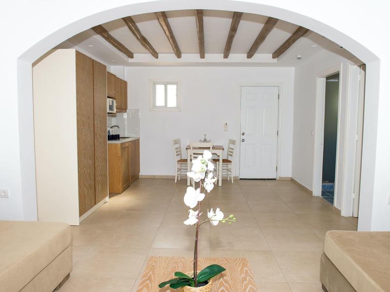 Blick durch einen Bogen in einen einfachen, hellen Wohn- und Küchenbereich mit Holzbalkendecke.