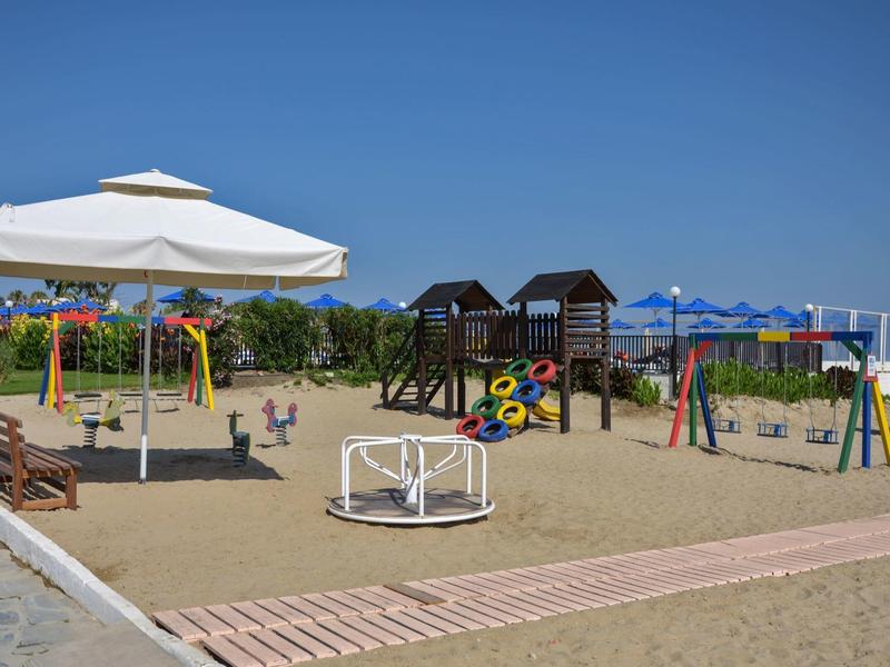 Kinderspielplatz am Strand mit Sand, Spielgeräten und Sonnenschirmen unter blauem Himmel