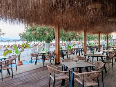 Otwarta restauracja z drewnianymi krzesłami i stołami pod strzechą nad morzem