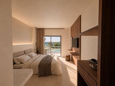 Modern eingerichtetes Hotelzimmer mit großem Bett und Meerblick durch Fenster.