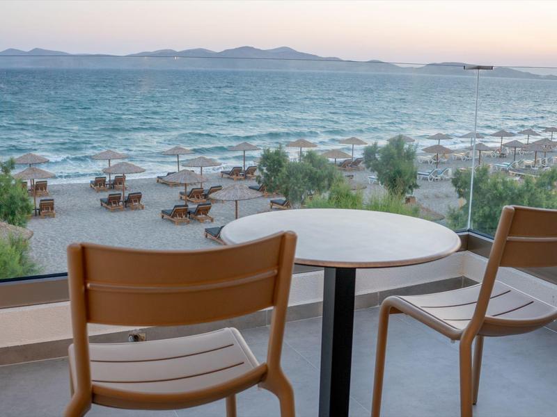 Zwei Holztische und Stühle auf Balkon mit Blick aufs Meer und Strand mit Liegen und Sonnenschirmen.