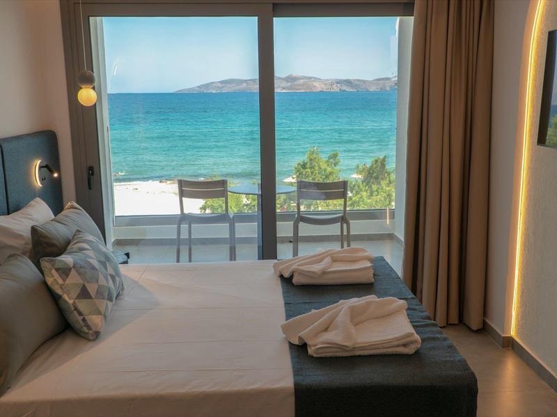 Modernes Schlafzimmer mit großem Bett, Meerblick durch Glasfenster, bequemen Kissen und neutralen Farben.