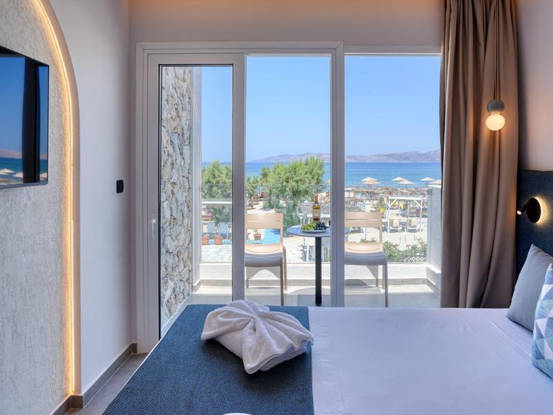 Hell eingerichtetes Schlafzimmer mit Doppelbett und Balkon mit Meerblick und Sitzgruppe.