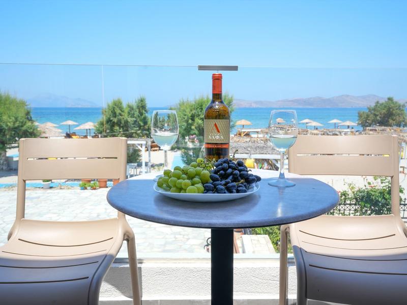 Tisch mit zwei Stühlen, Weinflasche, Weintrauben und Gläser, Meer und Himmel im Hintergrund.